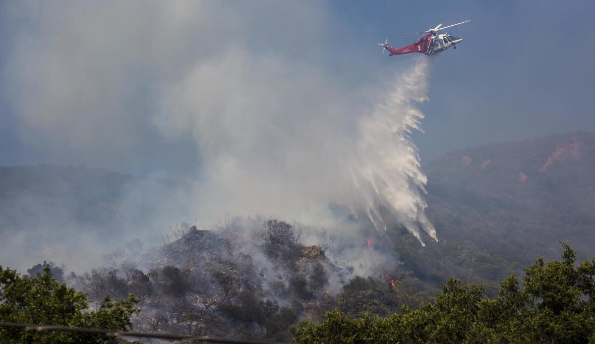 A Los Angeles Fire Department helicopter drops water on a brush fire near Topanga Canyon Boulevard north of Pacific Coast Highway in Malibu on Thursday afternoon.