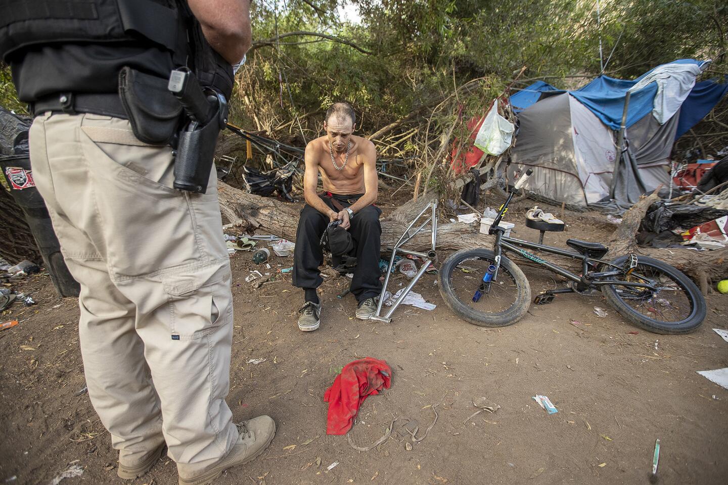 Officer Gabe Ricci with the Huntington Beach Homeless Task Force, left, talks with in Daniel Higgins near an encampement off of Ellis Ave in Huntington Beach on Wednesday, September 19.