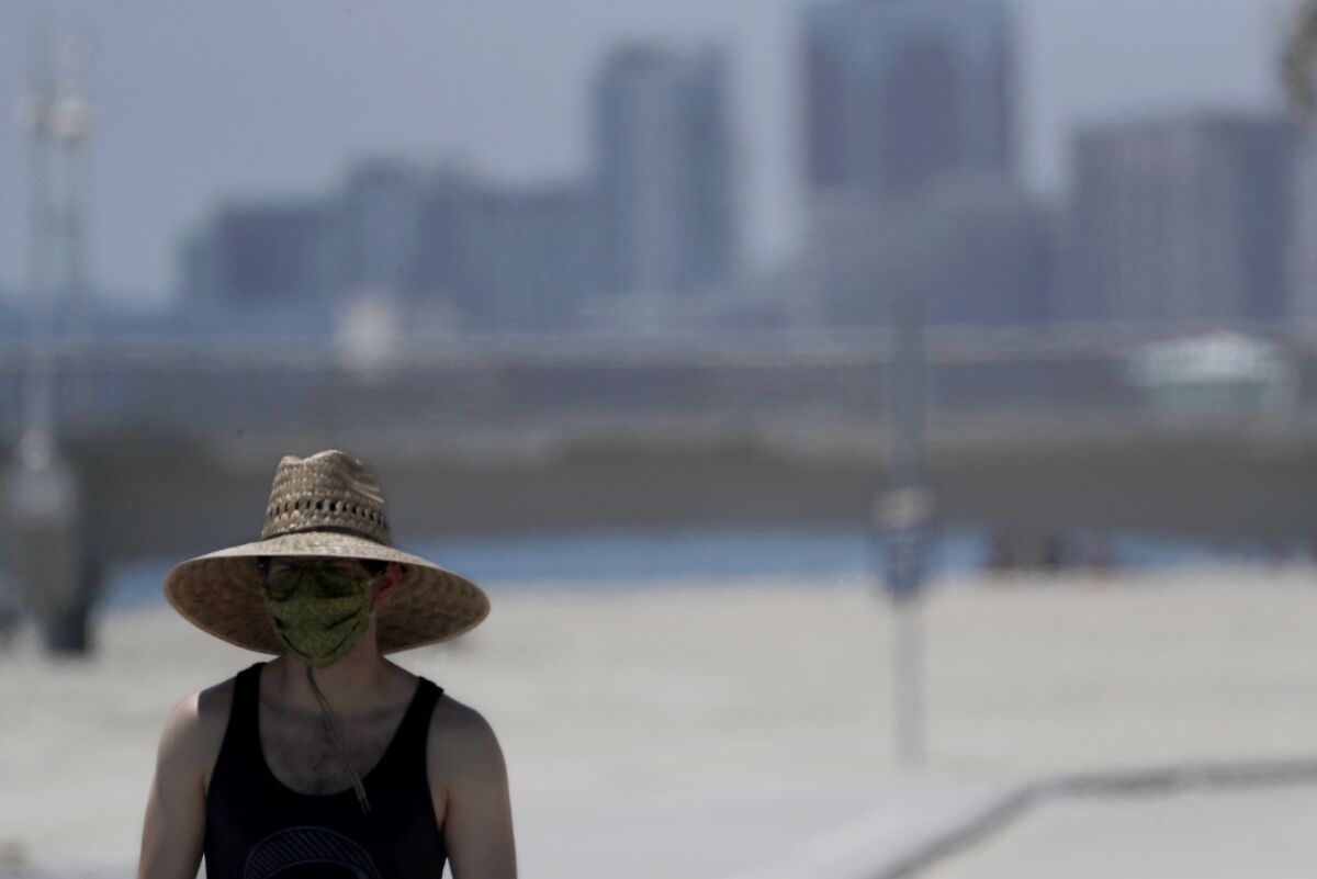 A man wears a mask and wide-brimmed hat as he walks along Junipero Beach in Long Beach on June 11.