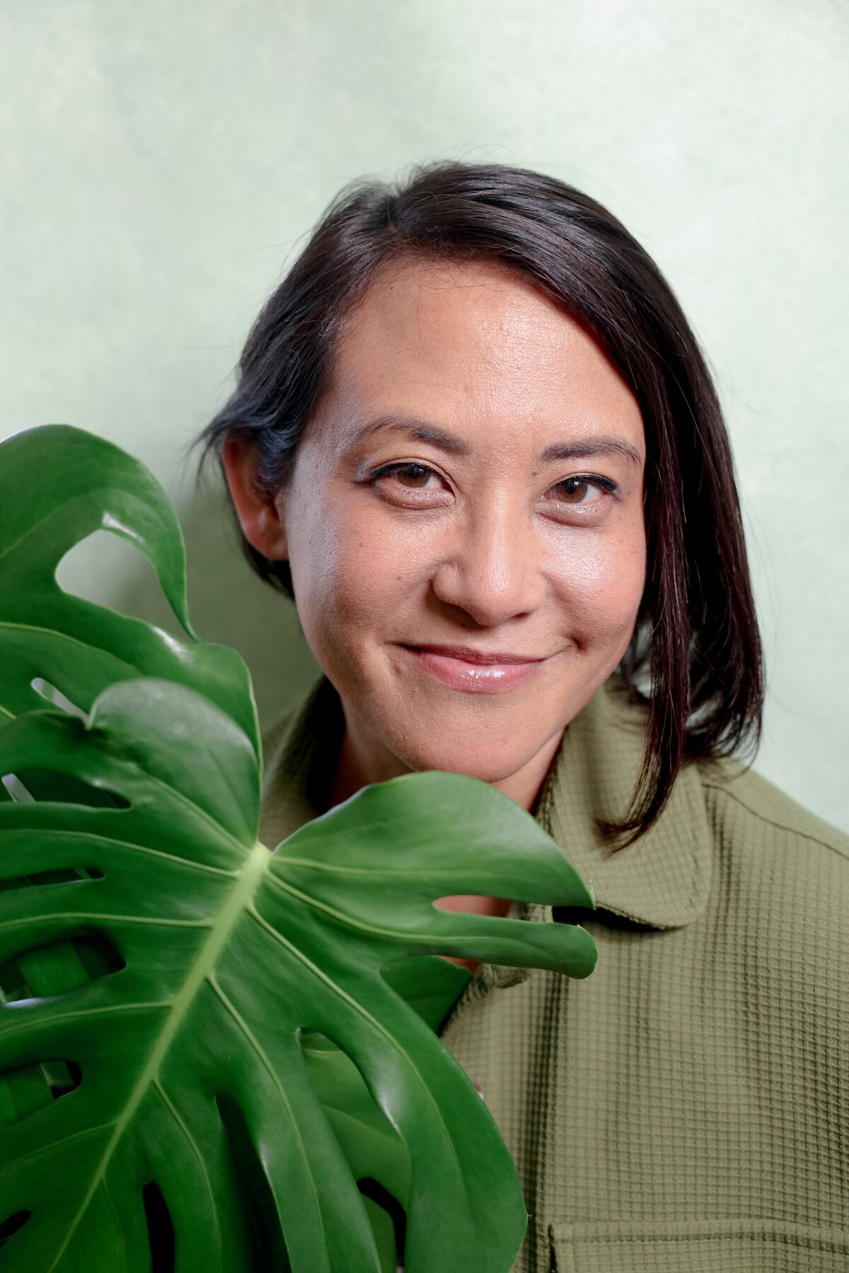 A woman with short, dark hair smiles at the camera while holding a plant.