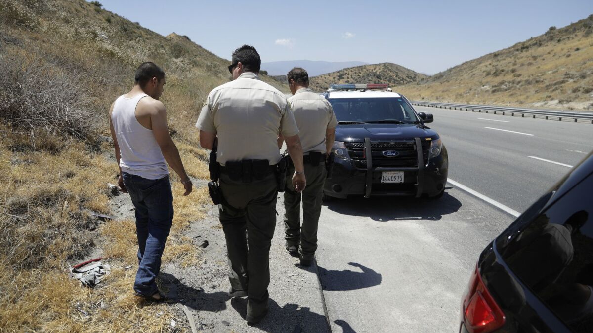 Los Angeles County Sheriff's Deputies Michael Vann, center, and John Leitelt take a driver to wait in a patrol car so they can search his car after he consented to a search. Upon completion of the search, he was released.