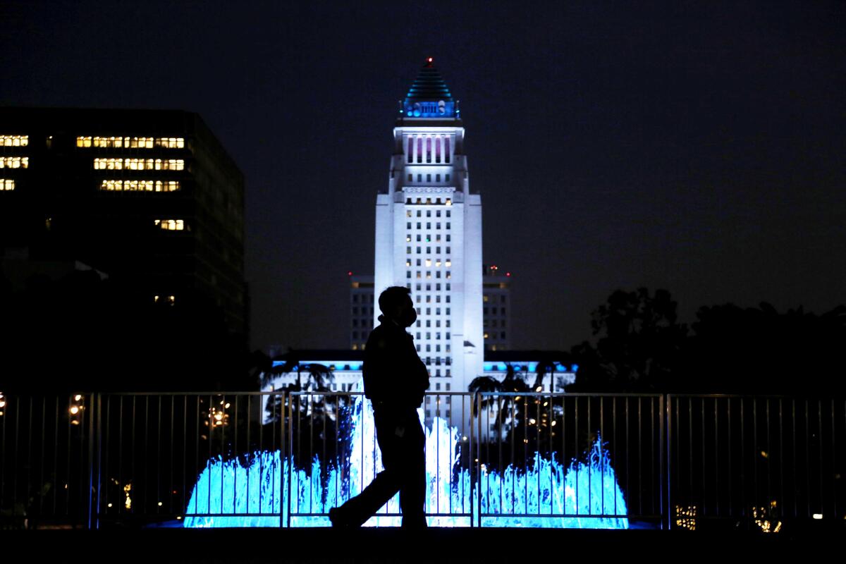 Los Angeles' City Hall from Grand Park at night while a pedestrian walks by in silhouette.