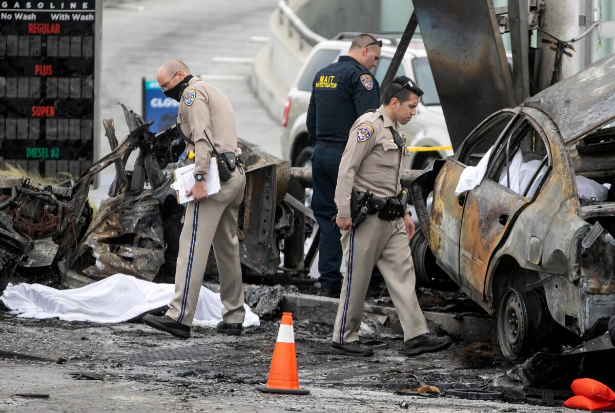 Officials examine the charred wreckage of a crash near a gas station