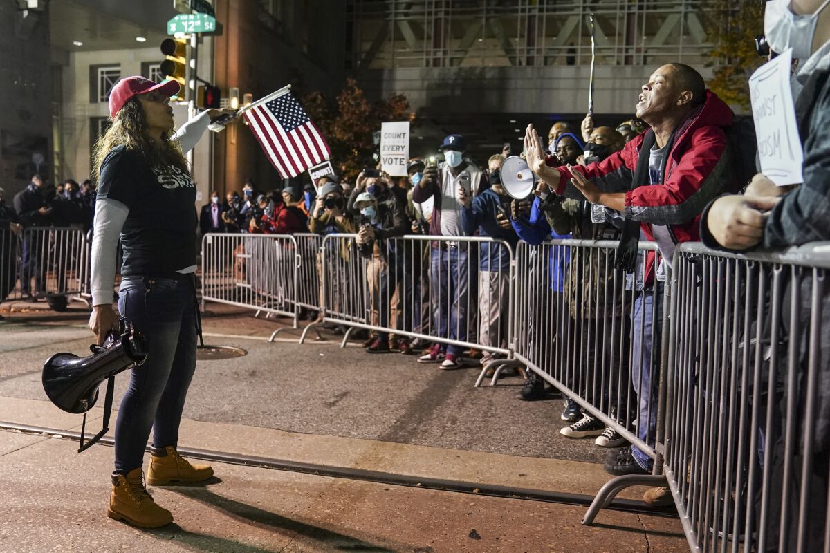A person with a megaphone talks to people behind a metal barrier