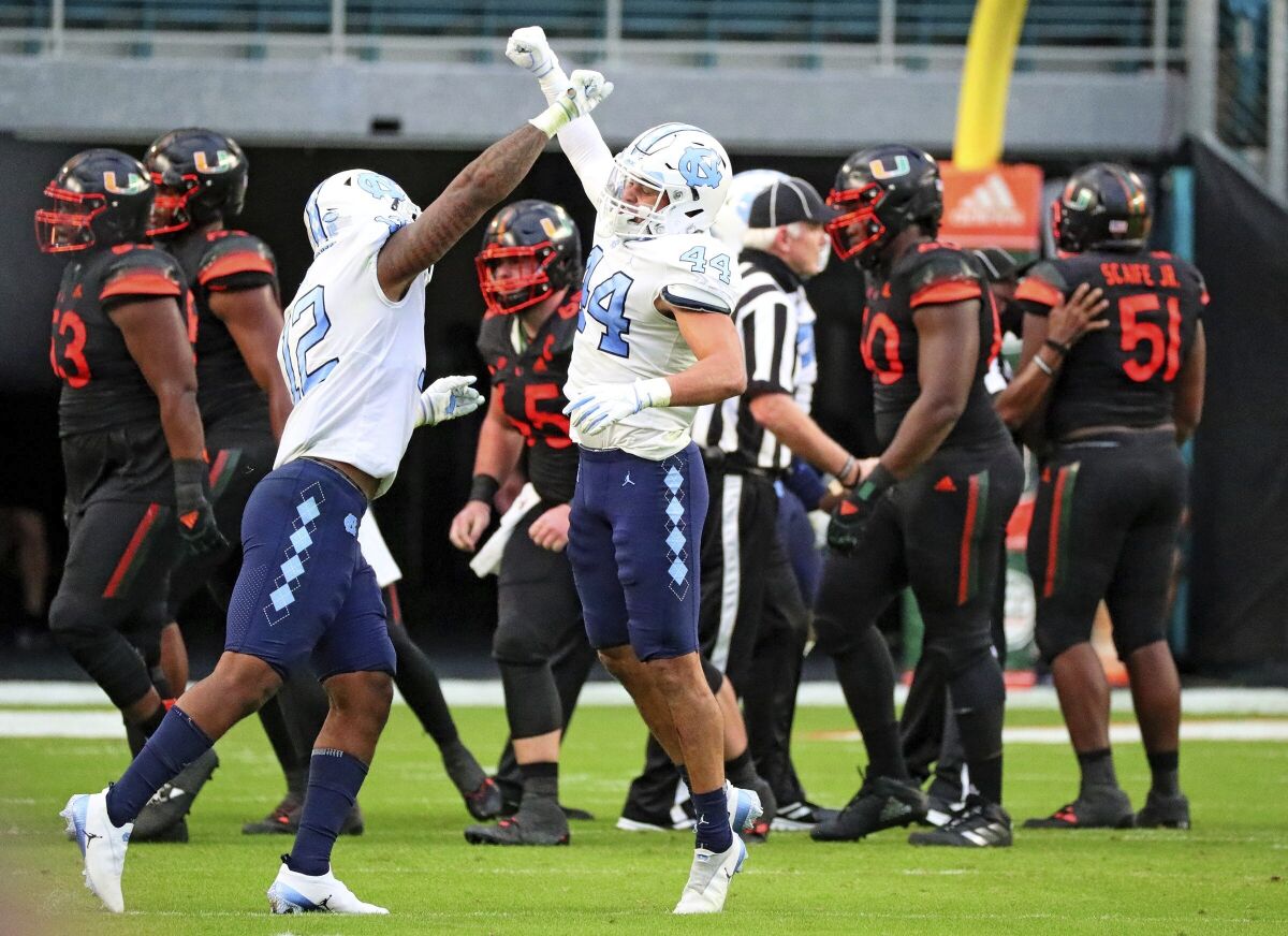 North Carolina linebackers Tomon Fox (12) and Jeremiah Gemmel (44) celebrate a stop against Miami during the first half of an during an NCAA college football game at Hard Rock Stadium In Miami Gardens, Fla, Saturday, Dec, 12, 2020. (Al Diaz/Miami Herald via AP)