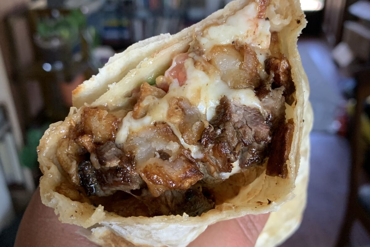 cross section of a burrito with steak, potatoes, cheese and pico de gallo. 
