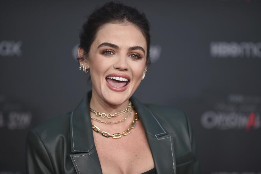 A woman with dark hair smiling with her mouth open while wearing a green leather jacket and gold chain necklaces