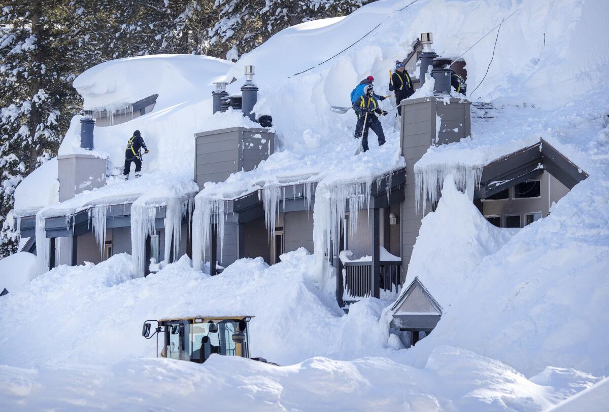 Workers shovel snow off the roofs of condos as a snowplow is dwarfed by snowdrifts while clearing the parking lot in Mammoth Lakes, Calif., after a blizzard dropped as much as 11 feet of snow in the biggest storm system so far this season.