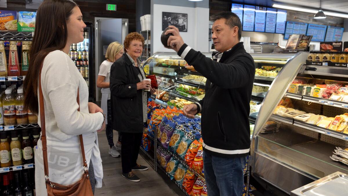 Co-owner David Wong selects an avocado for a customer Wednesday during the first day of business for the Irvine Ranch Market at 200 Marine Ave. on Balboa Island in Newport Beach.