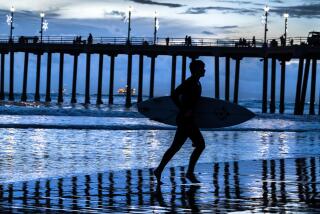 Huntington Beach, CA - December 31: A surfer and pier walkers enjoying the last day of 2023 are silhouetted by cloudy skies at dusk amid cool weather in Huntington Beach Sunday, Dec. 31, 2023. (Allen J. Schaben / Los Angeles Times)