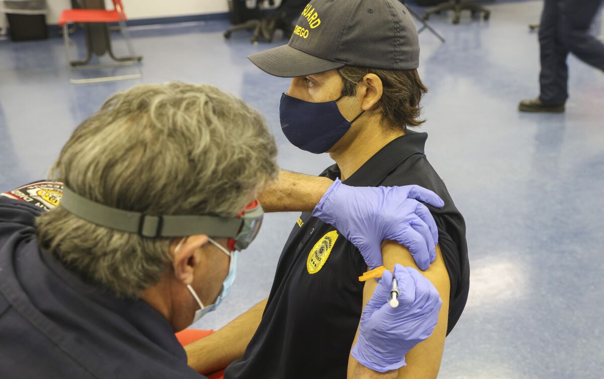 Firefighter/paramedic Mitch Mendler gives a COVID-19 vaccine to lifeguard Tarrant Seautelle.