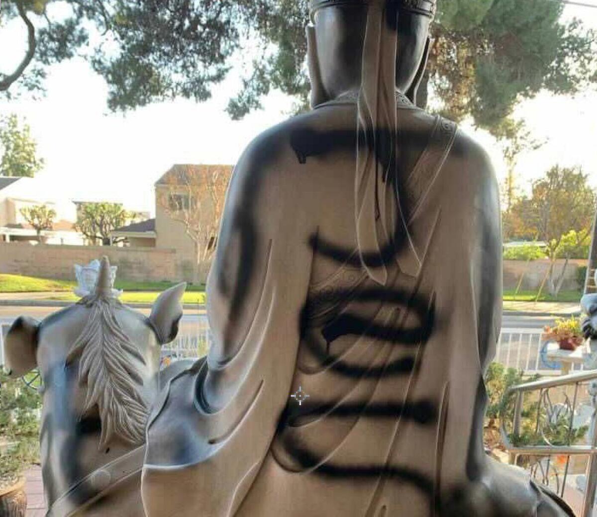 Black spray paint including the word "Jesus" on a Buddhist statue