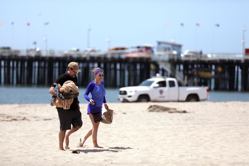SANTA CRUZ, CA -- MAY 22: Rick Tracewell, left, and partner Debi Tipple, both of Sacramento, are asked to leave Main Beach by the Santa Cruz Police Ranger on Friday, May 22, 2020, in Santa Cruz, CA. Santa Cruz has successfully bent the curve of cases and deaths from COVID-19 after sheltering in place early. The beaches will be closed from 11:00 a.m. to 5:00 p.m., daily until further notice. The ocean will remain open for water sports (e.g., surfing, boogie-boarding, swimming, paddle-boarding, kayaking, boating, etc.), and individuals may cross beaches in order to access and leave the ocean. All other non-exercise, passive, or sedentary activities at beaches, such as sitting, lying, standing, picnicking, etc, are prohibited. (Gary Coronado / Los Angeles Times)