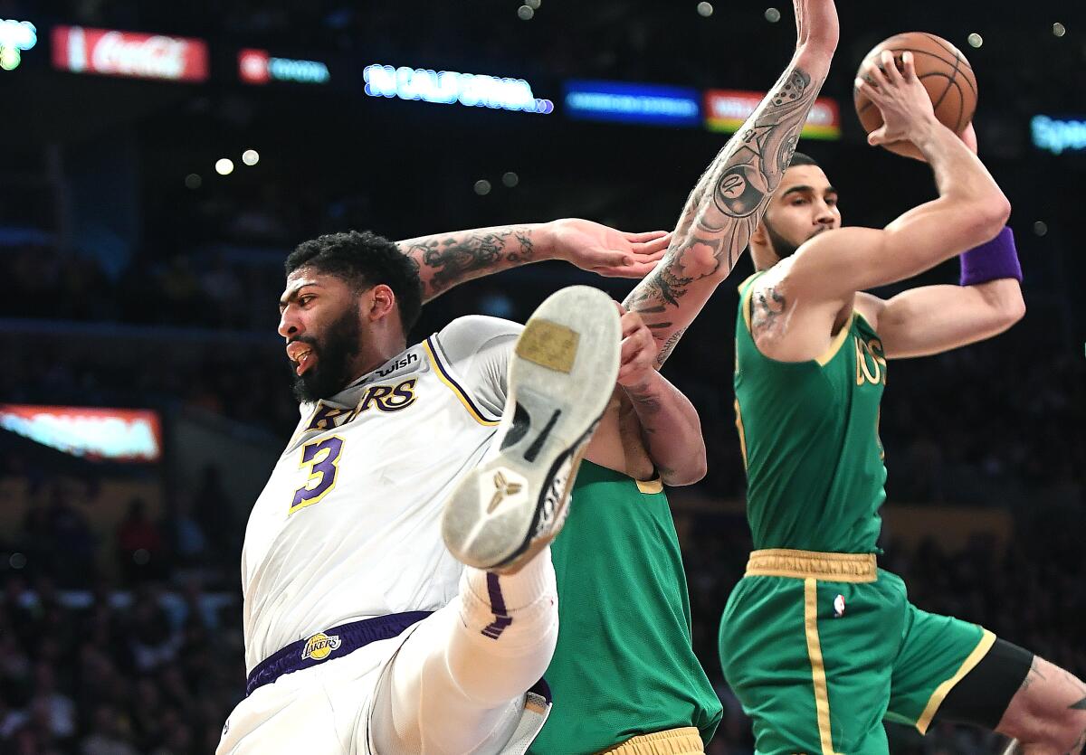 Lakers star Anthony Davis, left, battles with Celtics center Daniel Theis, center, as Jayson Tatum grabs the rebound during Sunday's game at Staples Center.