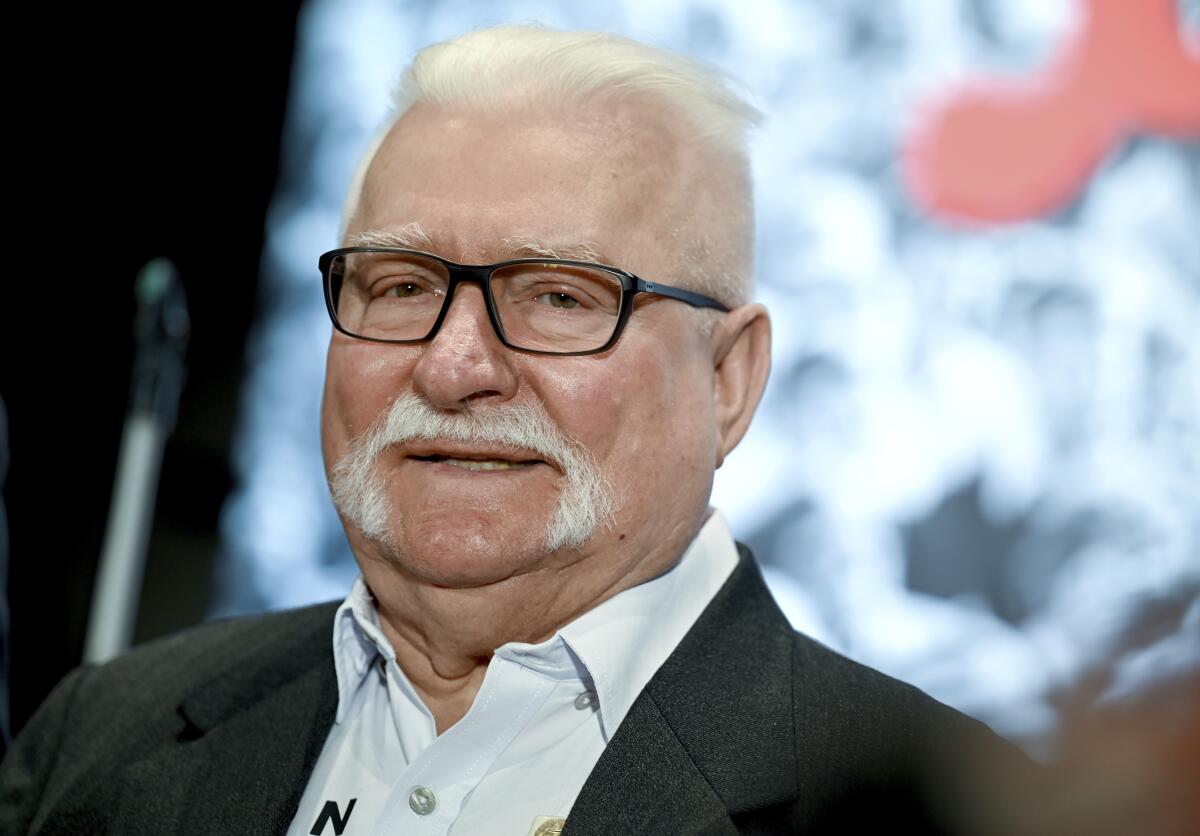 Lech Walesa smiles while wearing a white collared shirt and dark suit jacket