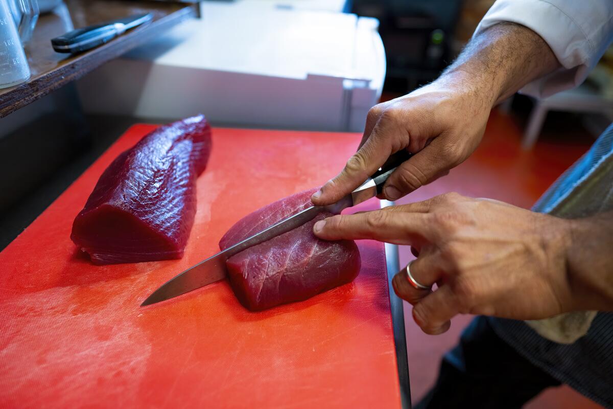 A chef slices a piece of sashimi-grade tuna on a cutting board in his kitchen.