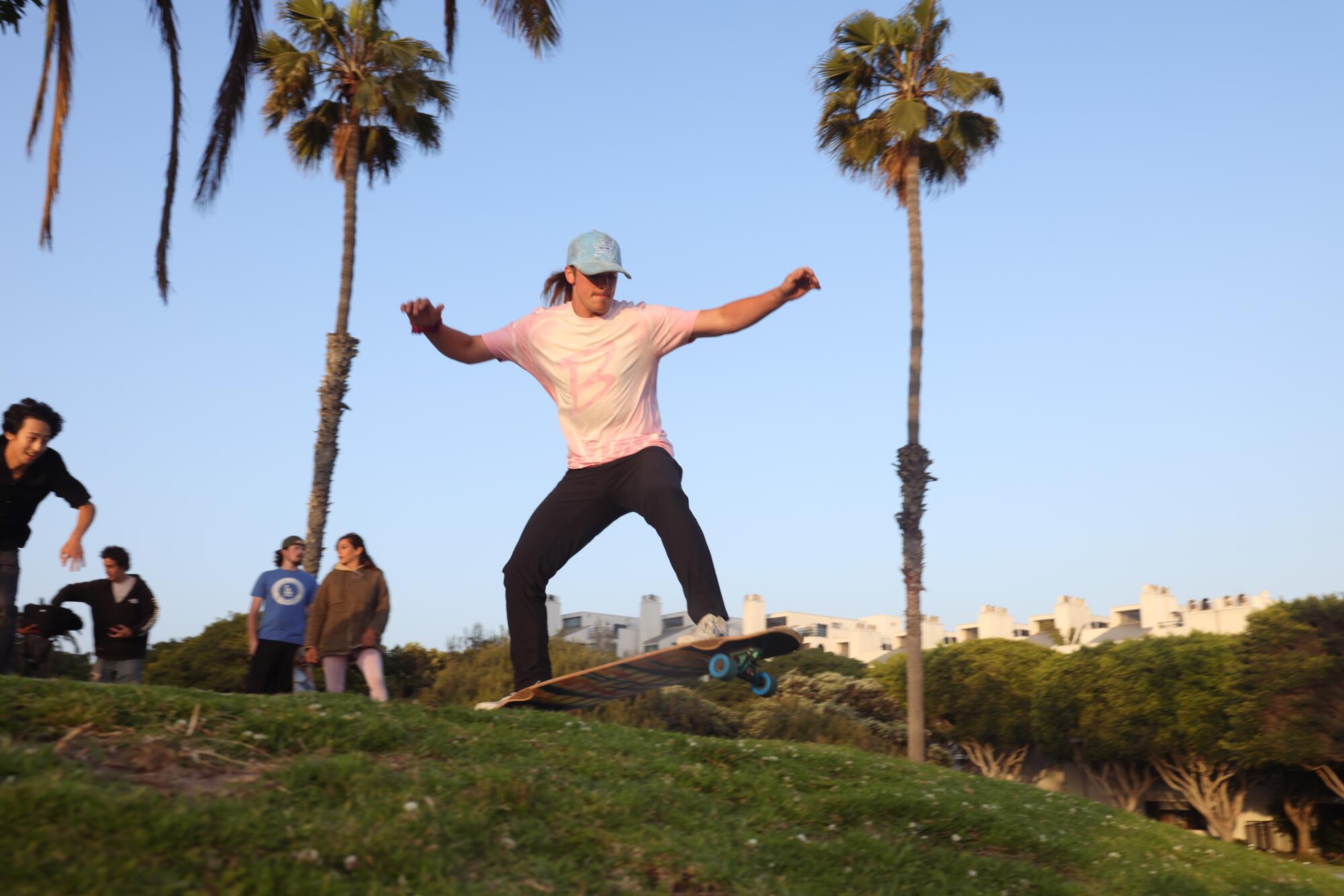 Brandon DesJarlais rides a skateboard down a grassy hill at a park