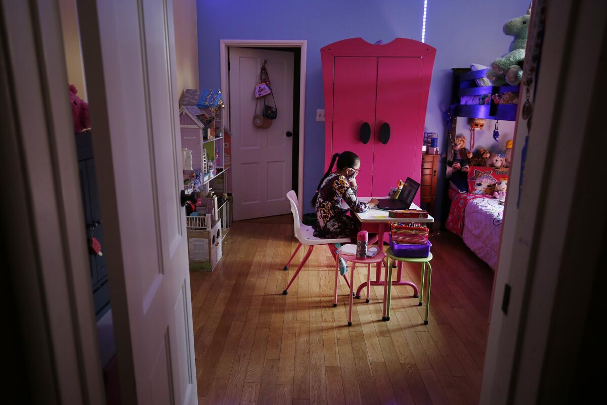 A young girl sits at a desk in her bedroom, using a laptop for virtual class