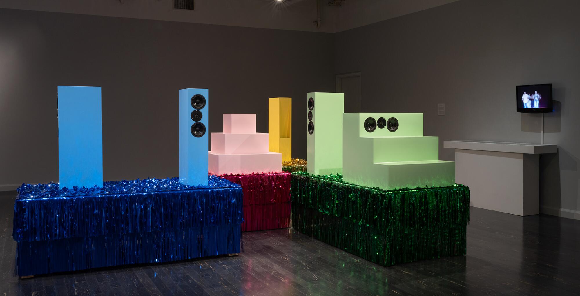 Speakers painted in candy shades are arranged on bring tinseled platforms in a work by Sonic Insurgency Research Group.