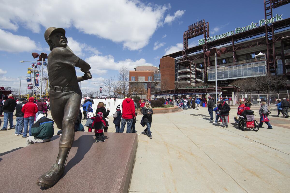 In this April 5, 2018 photo, fans mingle near a statue of Philadelphia Phillies' Mike Schmidt outside of Citizens Bank Park 