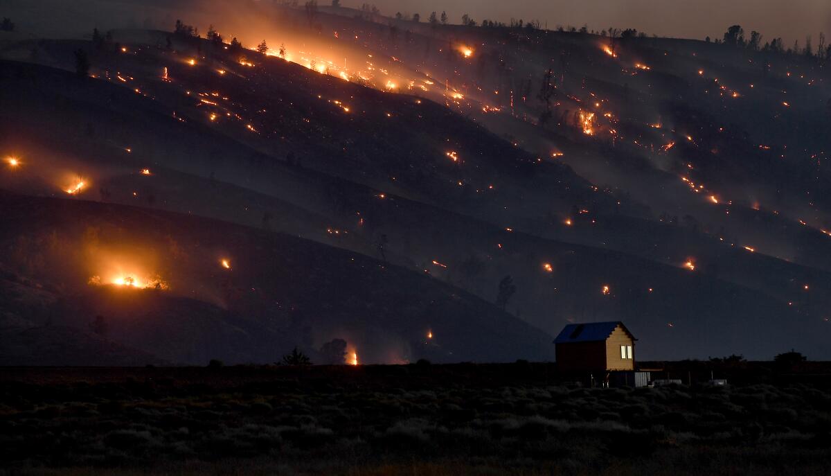 A solitary building stands in the foreground as the Lake fire burns in the hills of the Angeles National Forest behind it