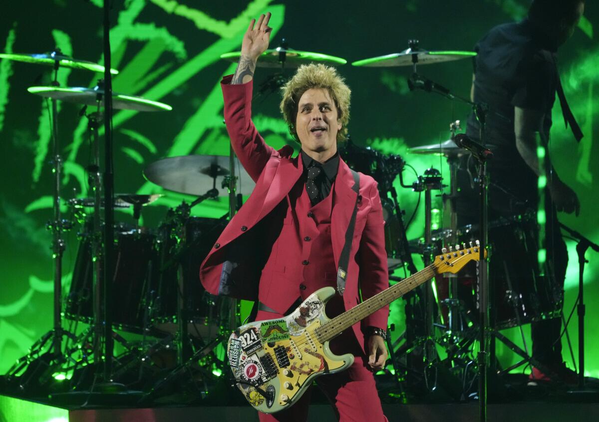 Billie Joe Armstrong of Green Day, in a red suit, onstage waving against a green-lighted background