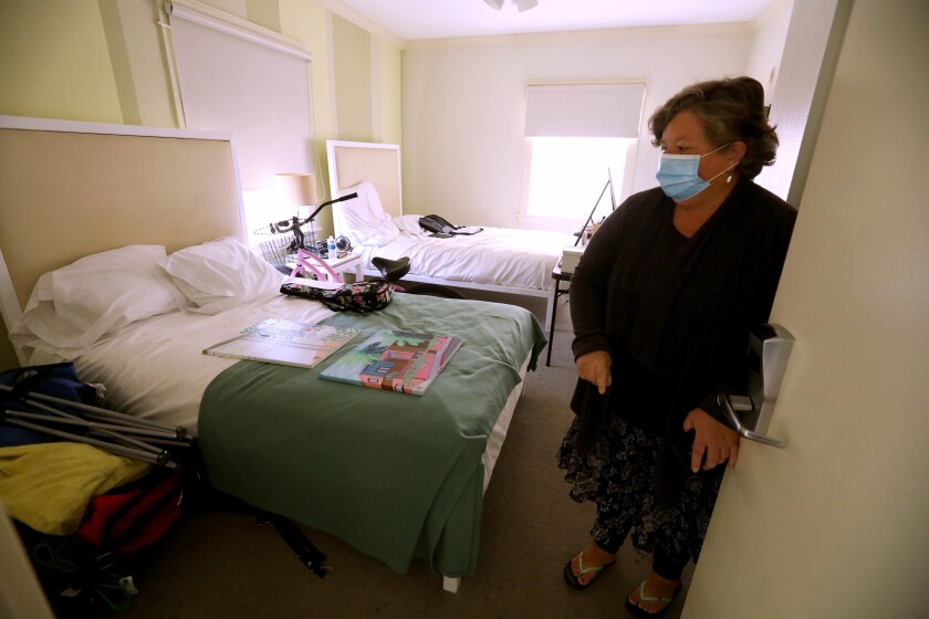 A masked person enters a room with two beds
