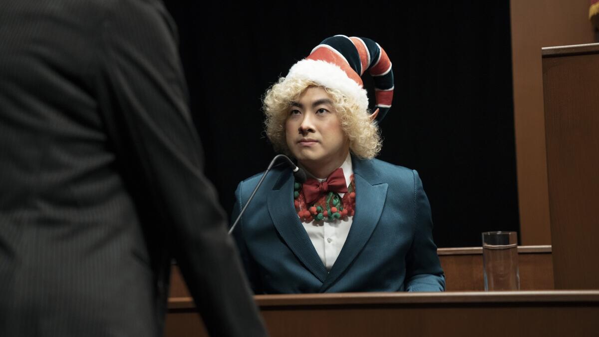 A man wearing an elf hat sitting on the witness stand in a courtroom.