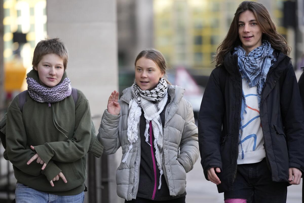 Greta Thunberg walks down a street flanked by two people, all of them in coats.