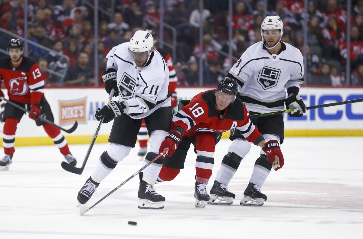 New Jersey Devils forward Ondrej Palat, center, reaches for the puck between Kings forward Anze Kopitar and Adrian Kempe.