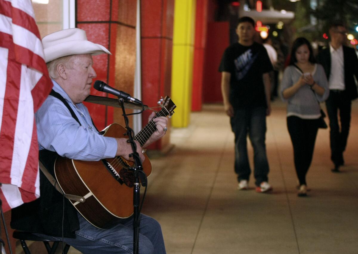 Street performer Red Benson plays folk rock on Brand Blvd. as people walk by, in Glendale on Saturday, January 25, 2014. Benson has been playing at this location for about 15 years.