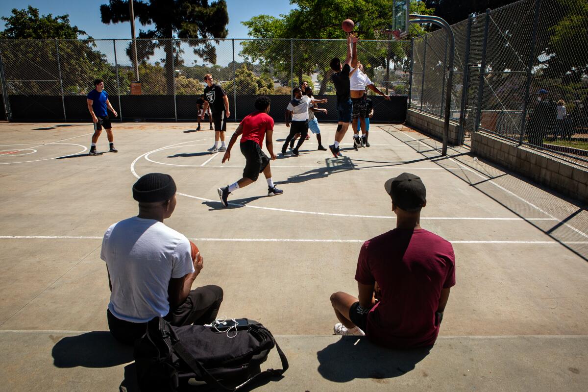 Two players sit and watch a pickup basketball game