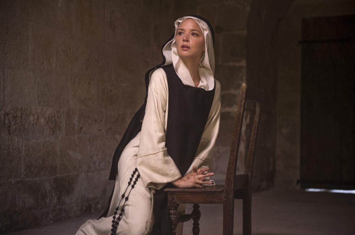 A woman in a nun's habit kneels in front of a chair.