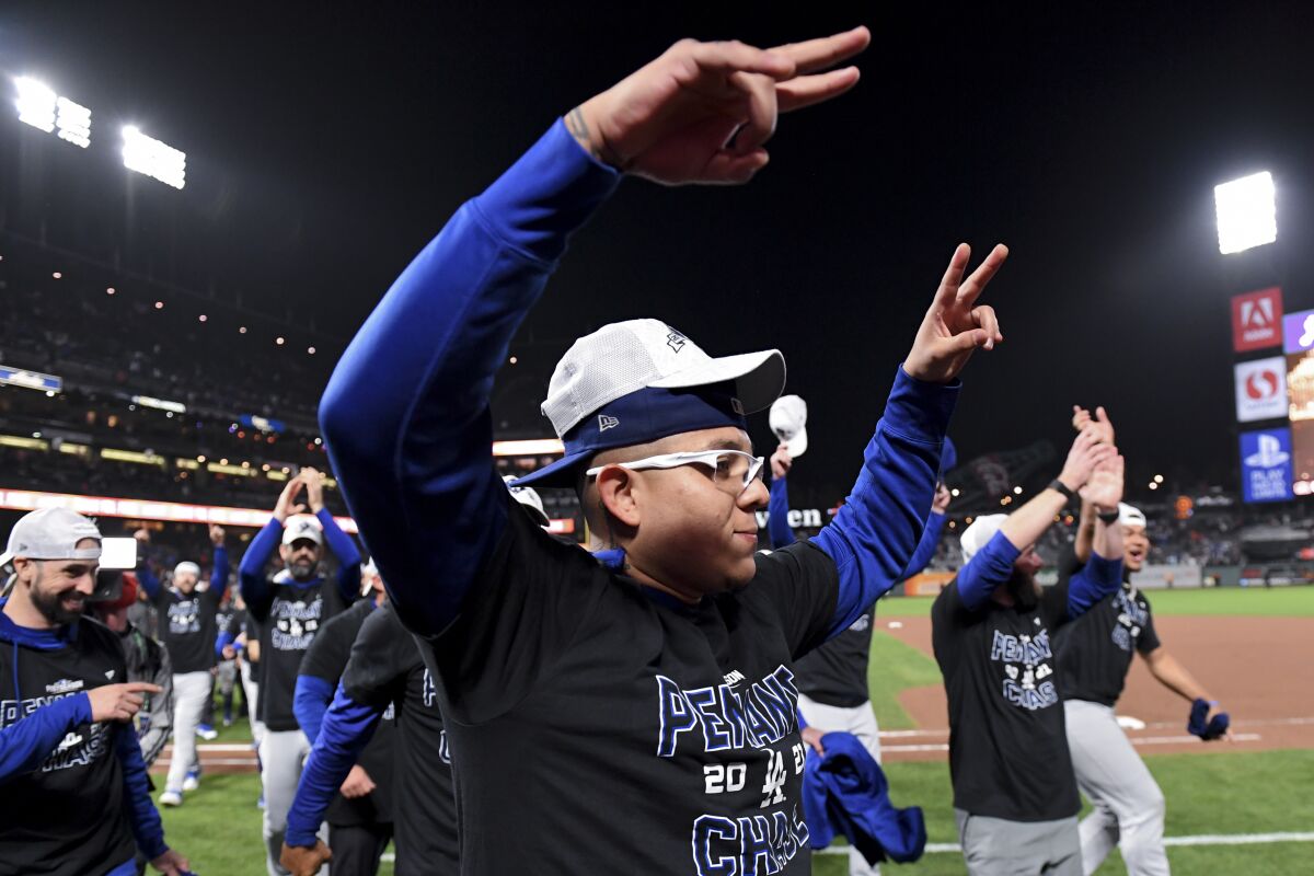 Dodgers pitcher Julio Urias lifts his arms in celebration while wearing two hats on his head