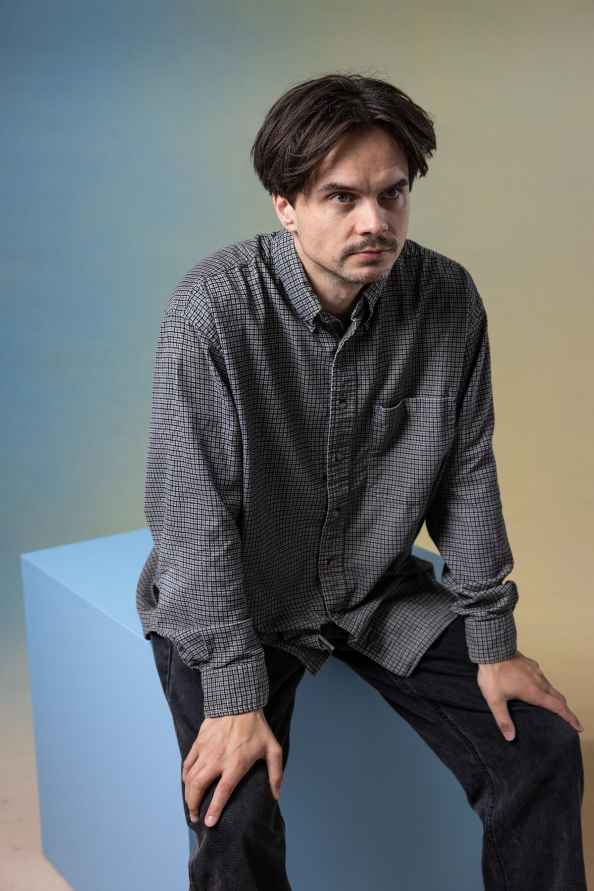 Kristoffer Borgli sits on a prop cube, hands on his knees for a portrait. 