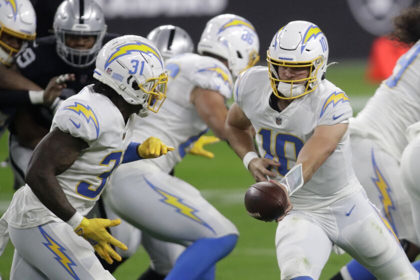 Los Angeles Chargers quarterback Justin Herbert (10) hands the ball off to Los Angeles Chargers running back Kalen Ballage (31) during the first half of an NFL football game against the Las Vegas Raiders, Thursday, Dec. 17, 2020, in Las Vegas. (AP Photo/Isaac Brekken)
