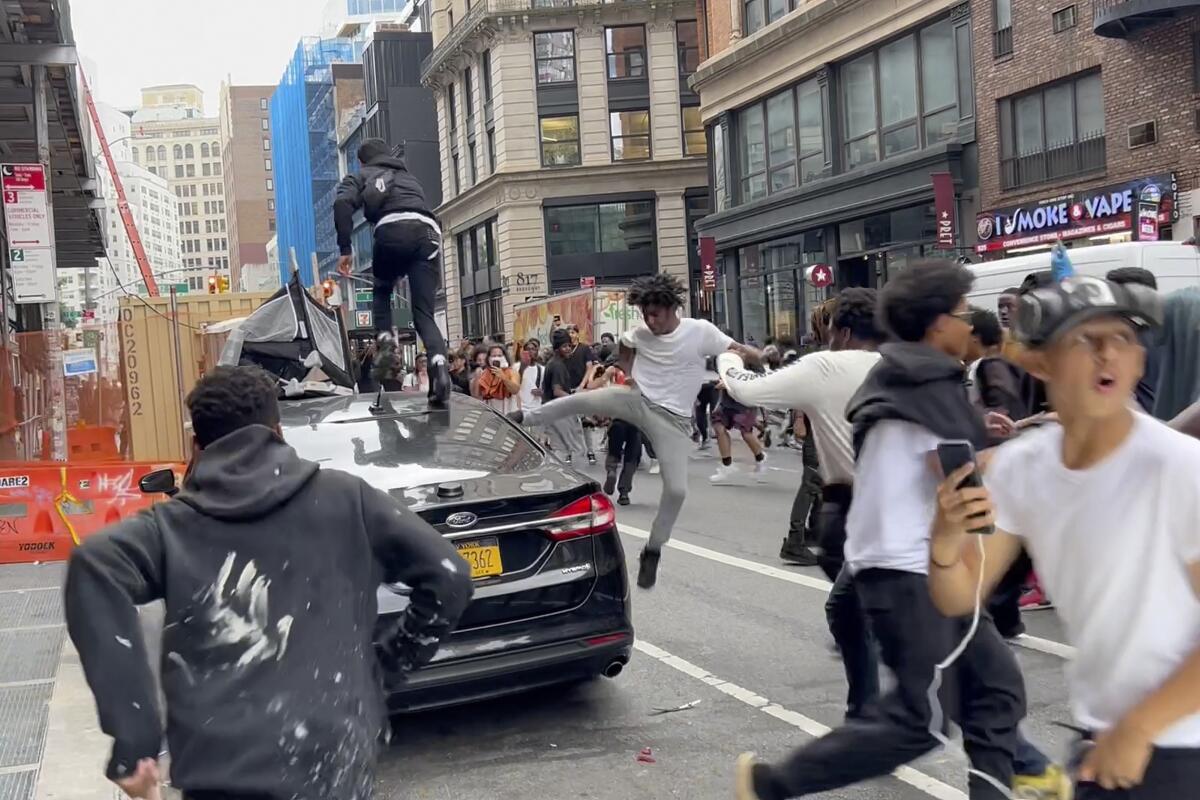 People jump and kick a car as a crowd runs through the street on Broadway near Union Square
