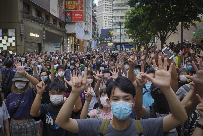 Masked crowds on a street hold up their fingers during a demonstration
