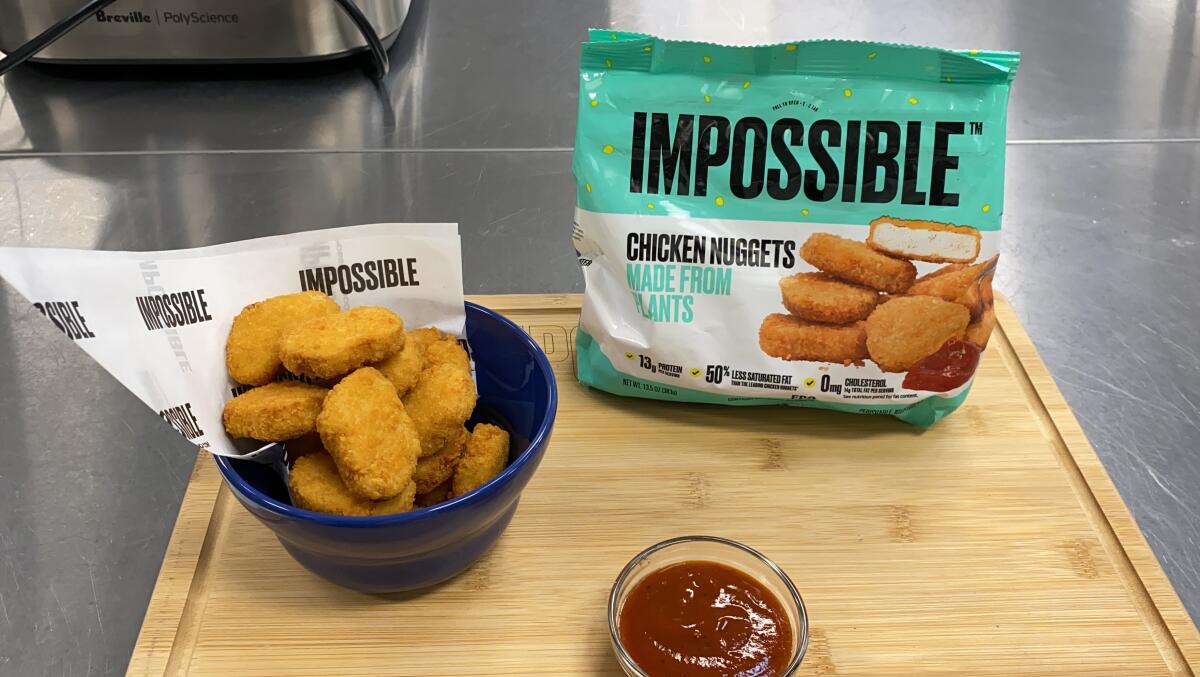 A bowl of meatless chicken nuggets rests on a table along with other items. A nearby bag has "Impossible" written on it.