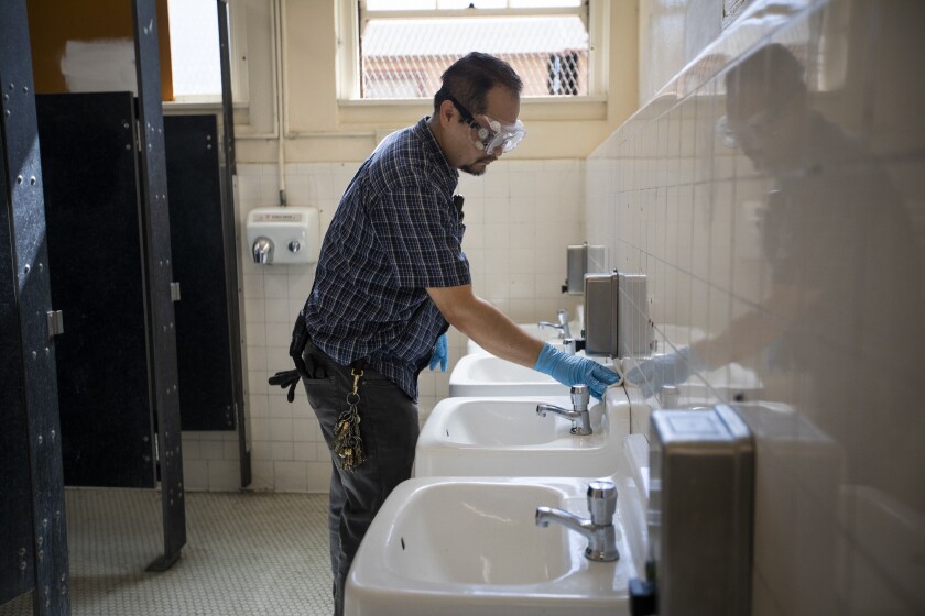 A man wipes down sinks in a school bathroom. 