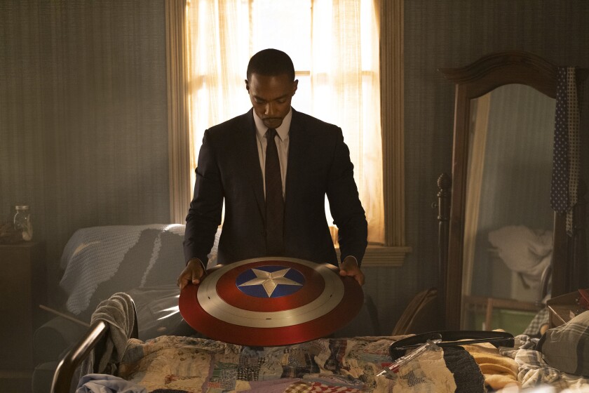 A Black man in a suit and tie holding Captain America's shield