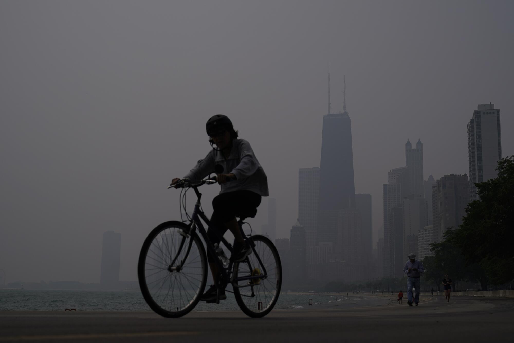 A cyclist riding in a dark haze against a partially obscured city skyline.