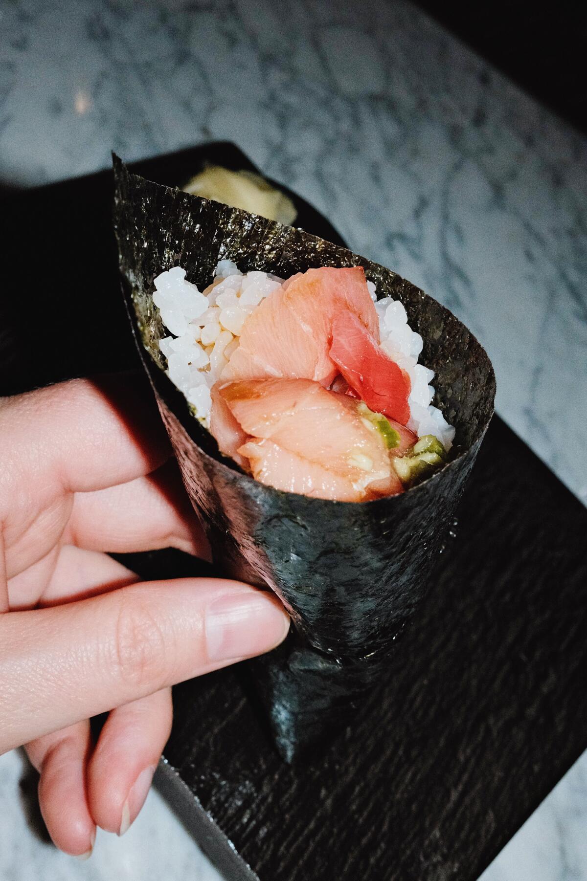 A vertical closeup of a hand holding a conical hand roll bursting with fish at Iki Nori sushi bar in Hollywood.