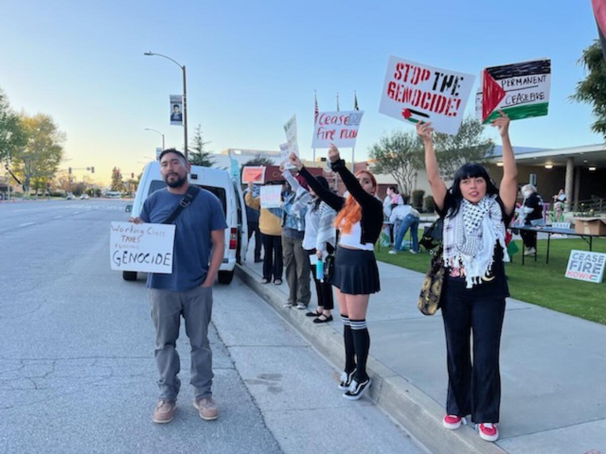 People holding signs stand at a curb