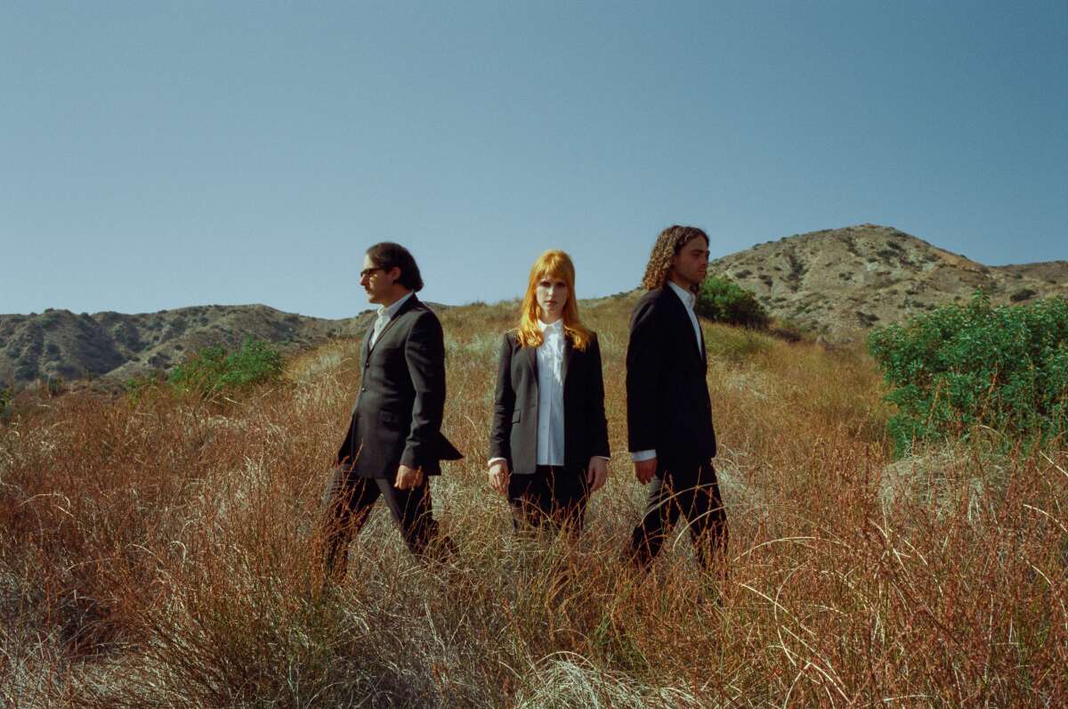 A three-piece rock band stands on a hillside.