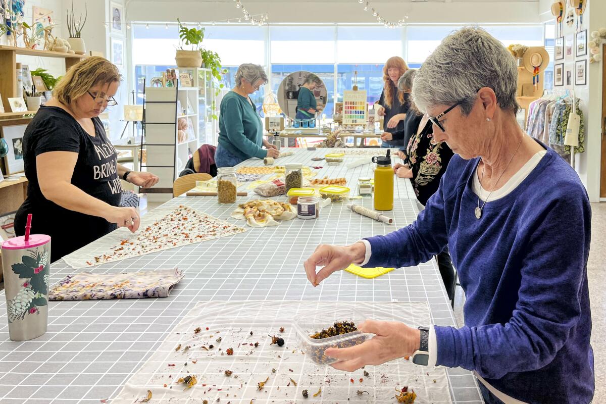 Students in a workroom sprinkle dried flowers on pieces of cloth.