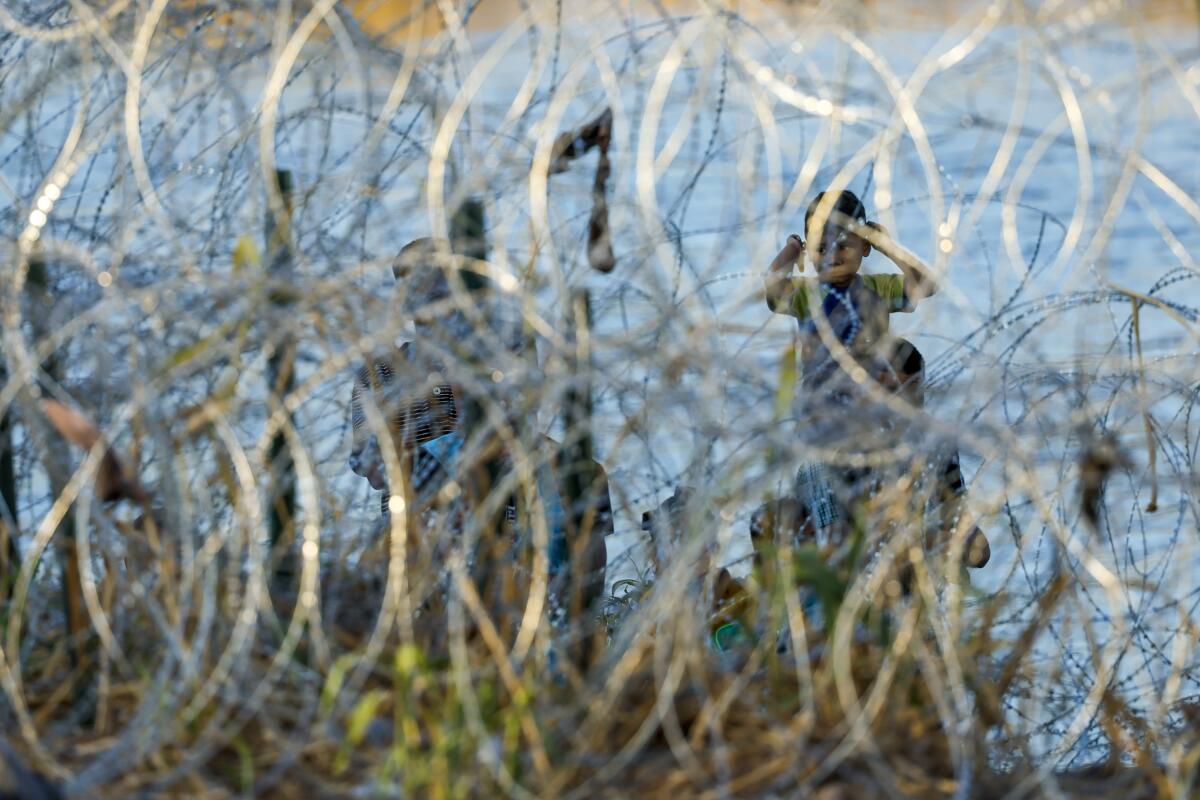 People stand behind razor wire along the Rio Grande.