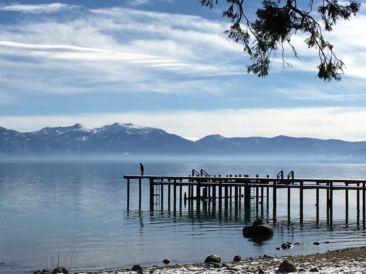 A figure stands on a dock out on the water of a lake.