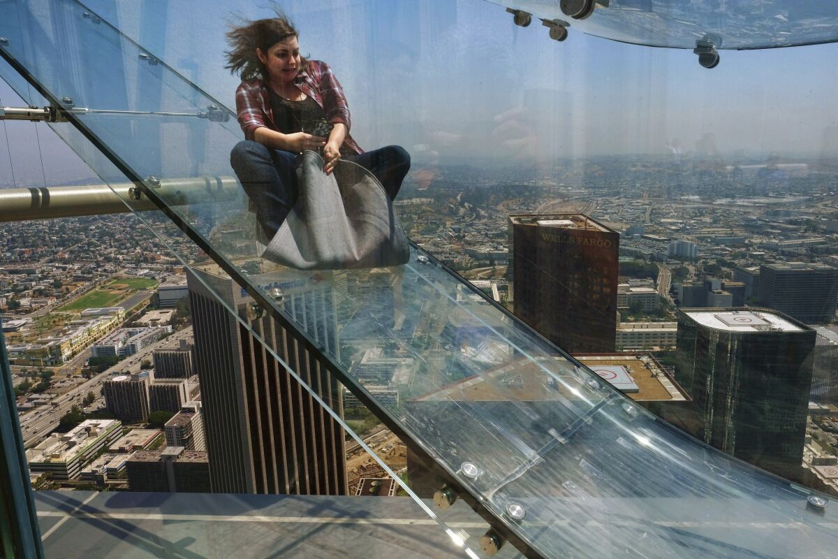 FILE - In this June 23, 2016, file photo, a member of the media rides down a glass slide during a media preview at the U.S. Bank Tower building in downtown Los Angeles. A renovation will do away with the Skyslide, located nearly a 1,000 feet high that gave thrill-seekers a brief ride on the outside of a downtown Los Angeles skyscraper. The new owner of the U.S. Bank Tower will remove the Skyslide and Skyspace public observation deck, the Los Angeles Times reported Friday, May 21, 2021. (AP Photo/Richard Vogel, File)