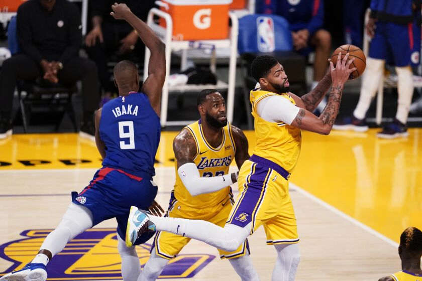 Lakers forward Anthony Davis grabs a rebound next to teammate LeBron James (23) and Clippers center Serge Ibaka on Tuesday.